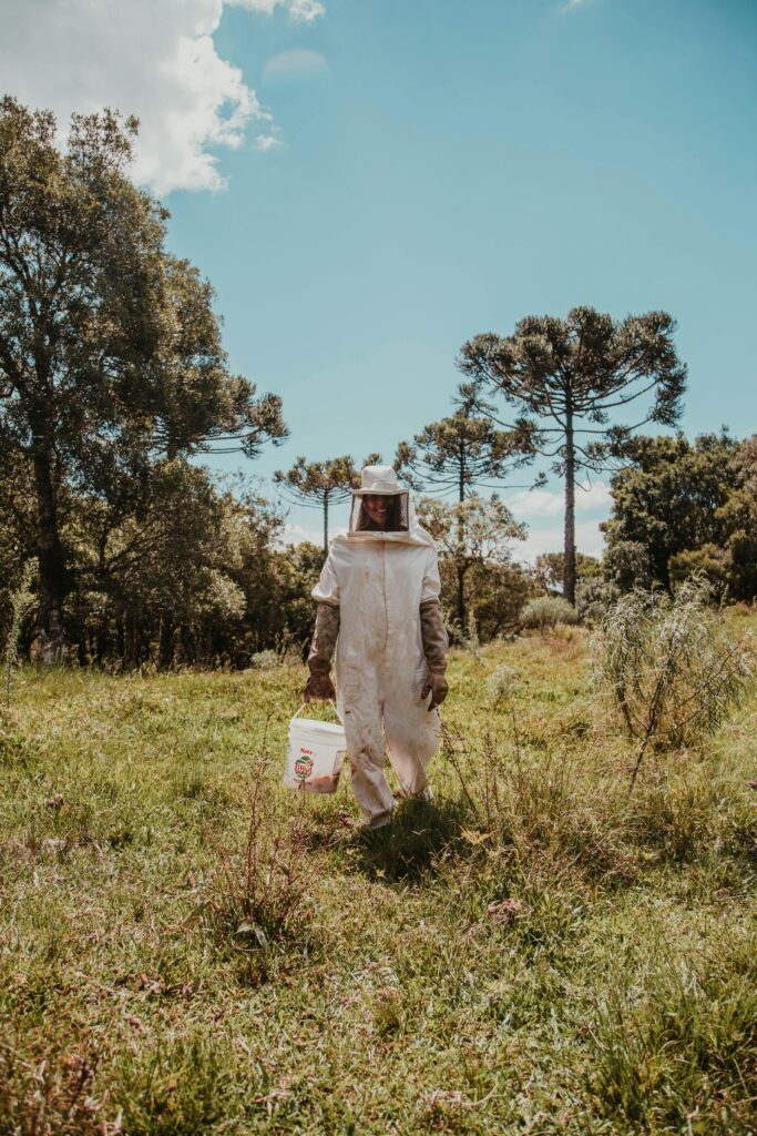 pexels-photo-2260936-2260936 A beekeeper in protective gear walking through a lush green field on a sunny day.