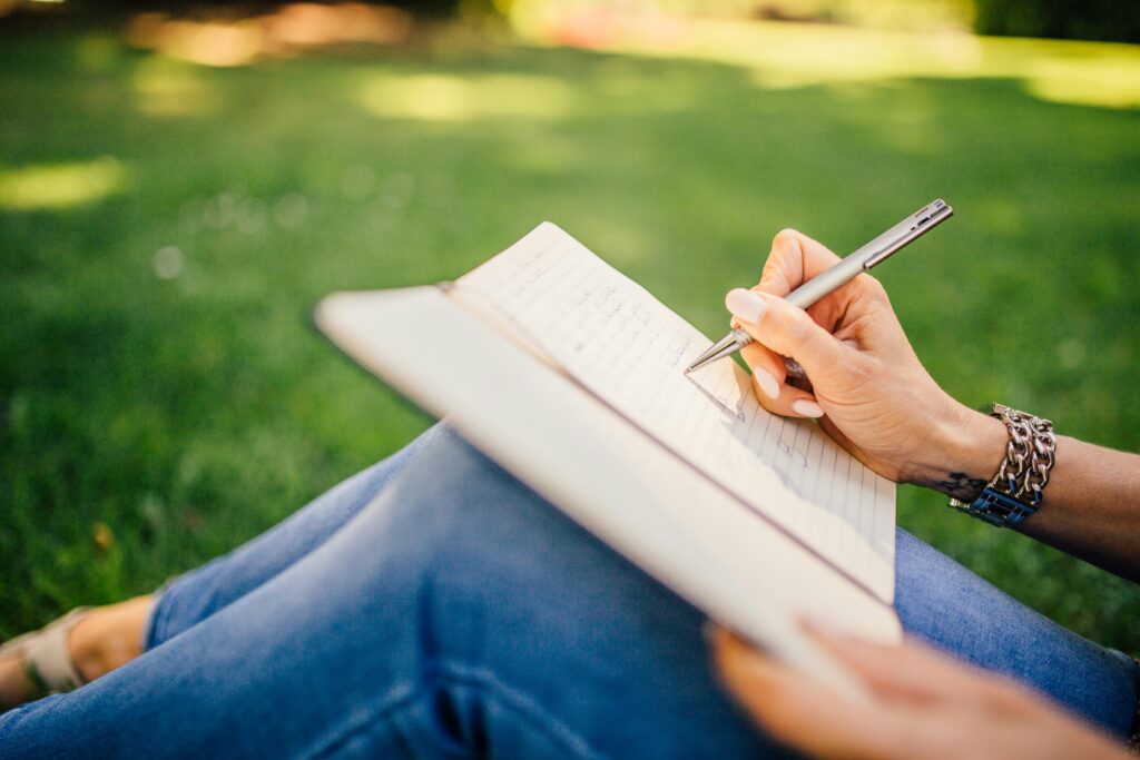 pexels-photo-34072 Person writes in a notebook on a sunny day. Focus on hands and pen outdoors.